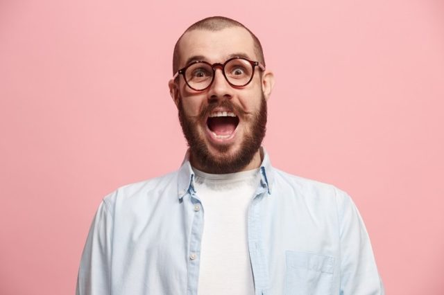 Hombre barbudo de aspecto sorprendido con camisa azul sobre fondo rosa