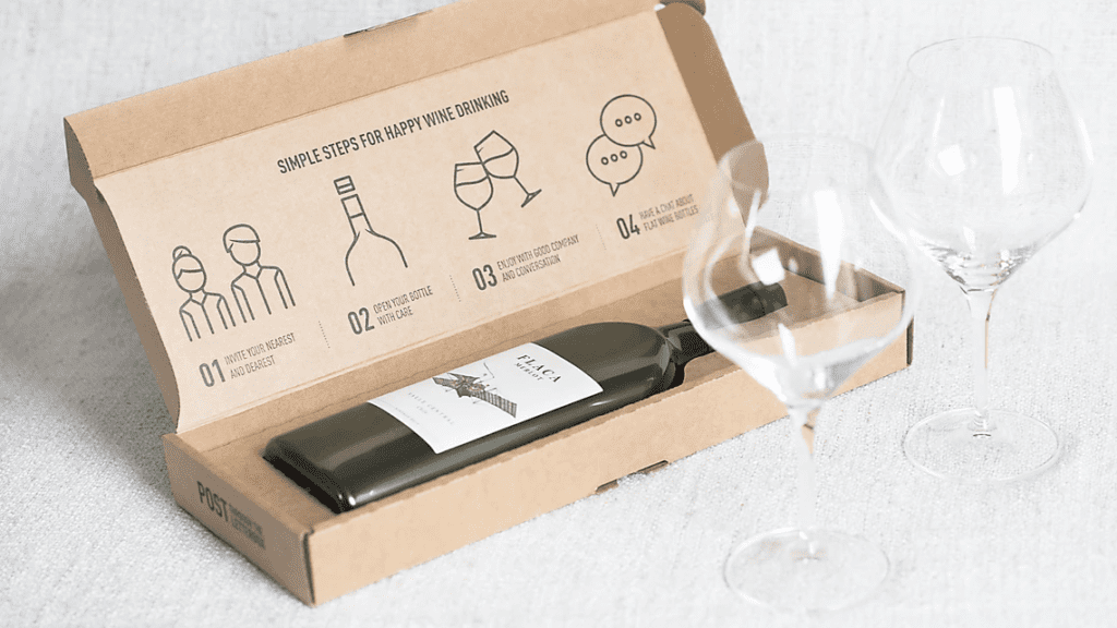 Wine bottle in cardboard box. Two empty wine glasses beside it.